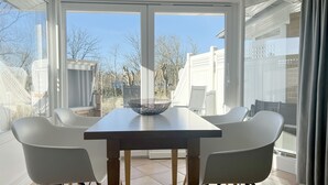 A dining area with a table and chairs, large windows, and a view of the neighborhood. - Luna16 (Room category) - Luna II (Sankt Peter-Ording)