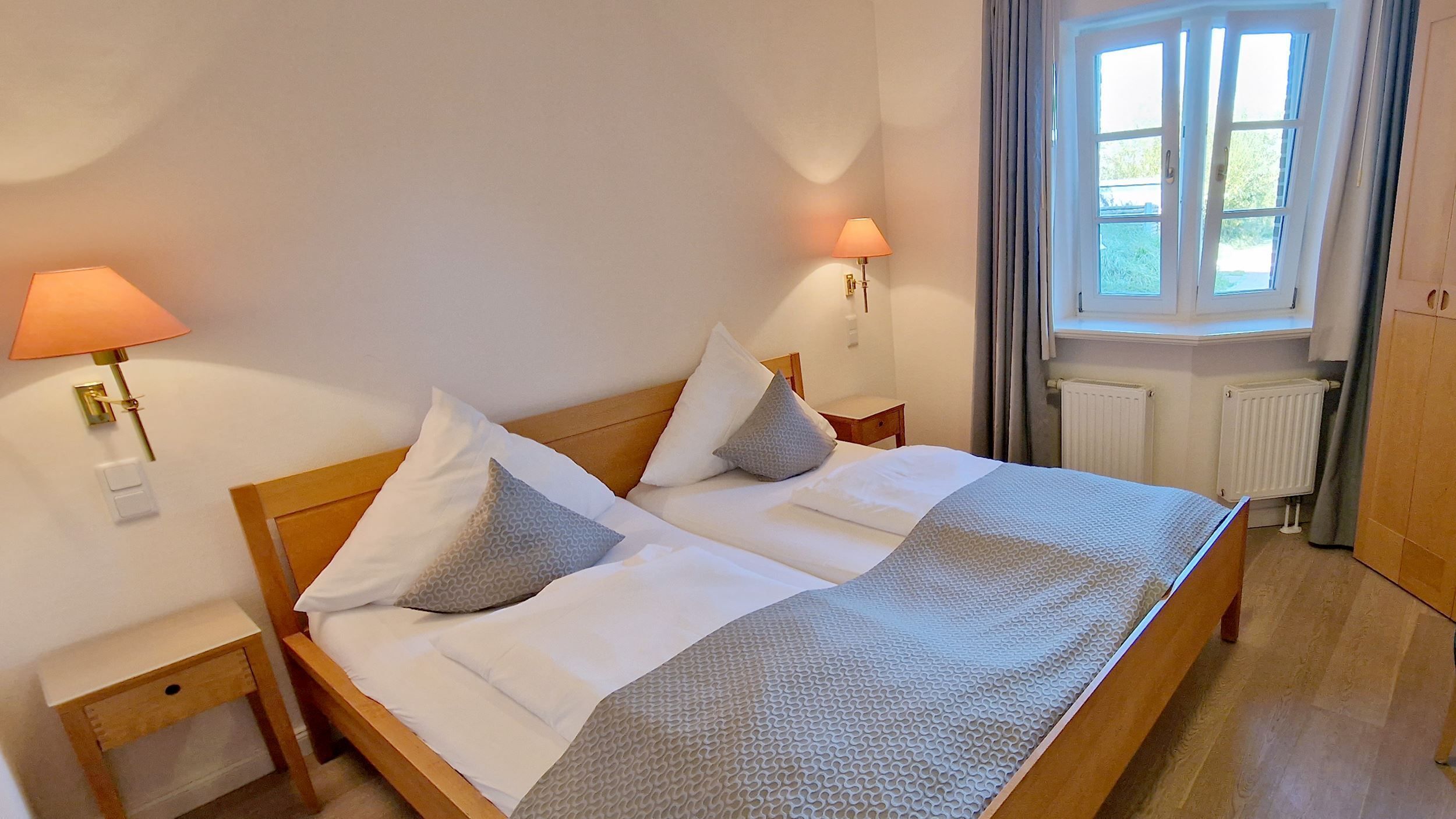 A double bed with a wooden frame, two bedside tables, a window with curtains, and a radiator.