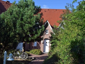 Une maison traditionnelle en briques, avec un toit recouvert de tuiles rouges, une porte blanche et un vélo garé devant.