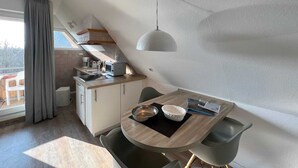 A compact kitchen with a dining area, a microwave, a coffee maker, and a hanging pendant light. - Luna34 (Room category) - Luna IV (Sankt Peter-Ording)