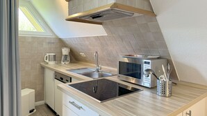 A modern kitchen with a built-in microwave, stove, sink, and coffee maker. - Luna34 (Room category) - Luna IV (Sankt Peter-Ording)