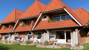 A row of houses with red-tiled roofs, a well-maintained lawn, and outdoor seating areas. - Luna34 (Room category) - Luna IV (Sankt Peter-Ording)