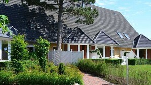 A row of traditional-style cottages with pitched roofs, a paved walkway, and well-maintained greenery. - Luna I - Luna Apartment 11 (Sankt Peter-Ording)