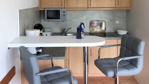 A compact kitchen with wooden cabinets, a microwave, a sink, and two grey chairs. - Luna I - Luna Apartment 11 (Sankt Peter-Ording)