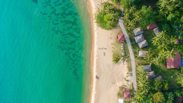 An aerial view of a beach resort with clear turquoise waters, a sandy shore, and several bungalow-style buildings with red roofs. - 1511 Coconut Grove (Tioman Island)