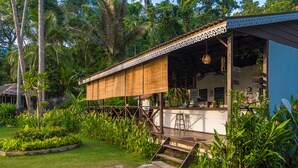 A rustic outdoor bar area with a wooden deck, surrounded by lush greenery and palm trees. - 1511 Coconut Grove (Tioman Island)