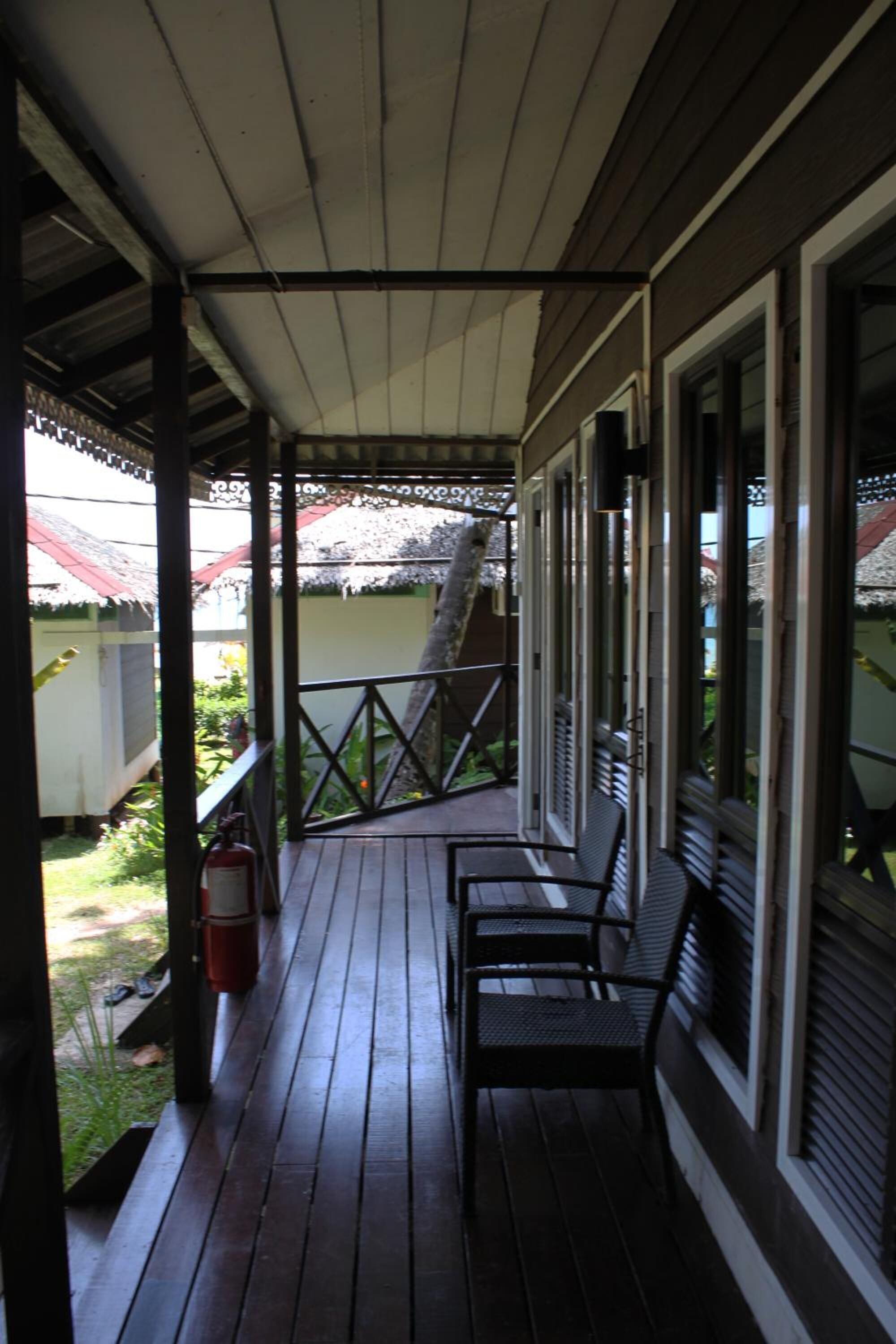 A covered porch with wooden flooring, metal railings, and a fire extinguisher.