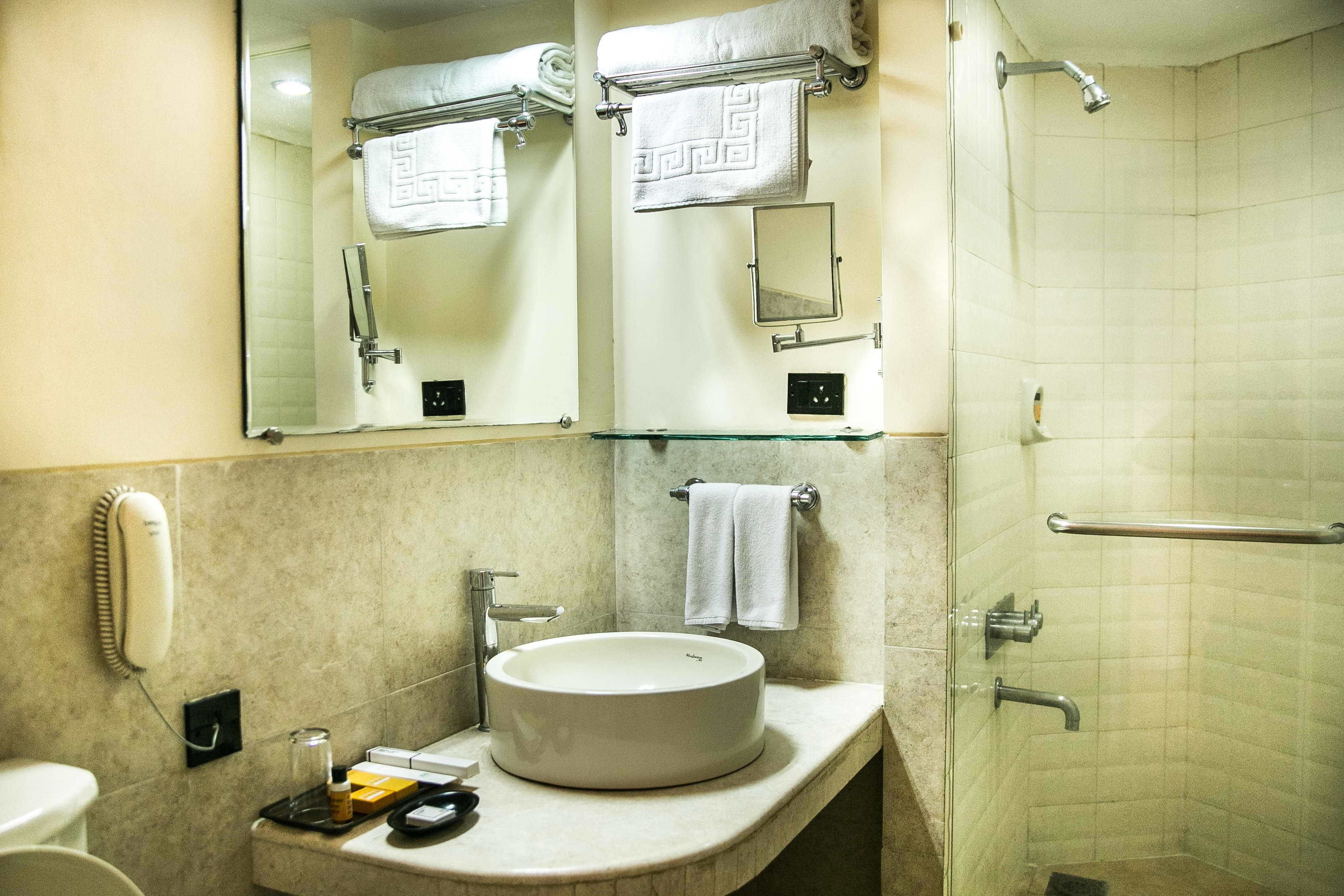 A bathroom with a round sink, a mirror, a towel rack, a shower, and a glass partition.