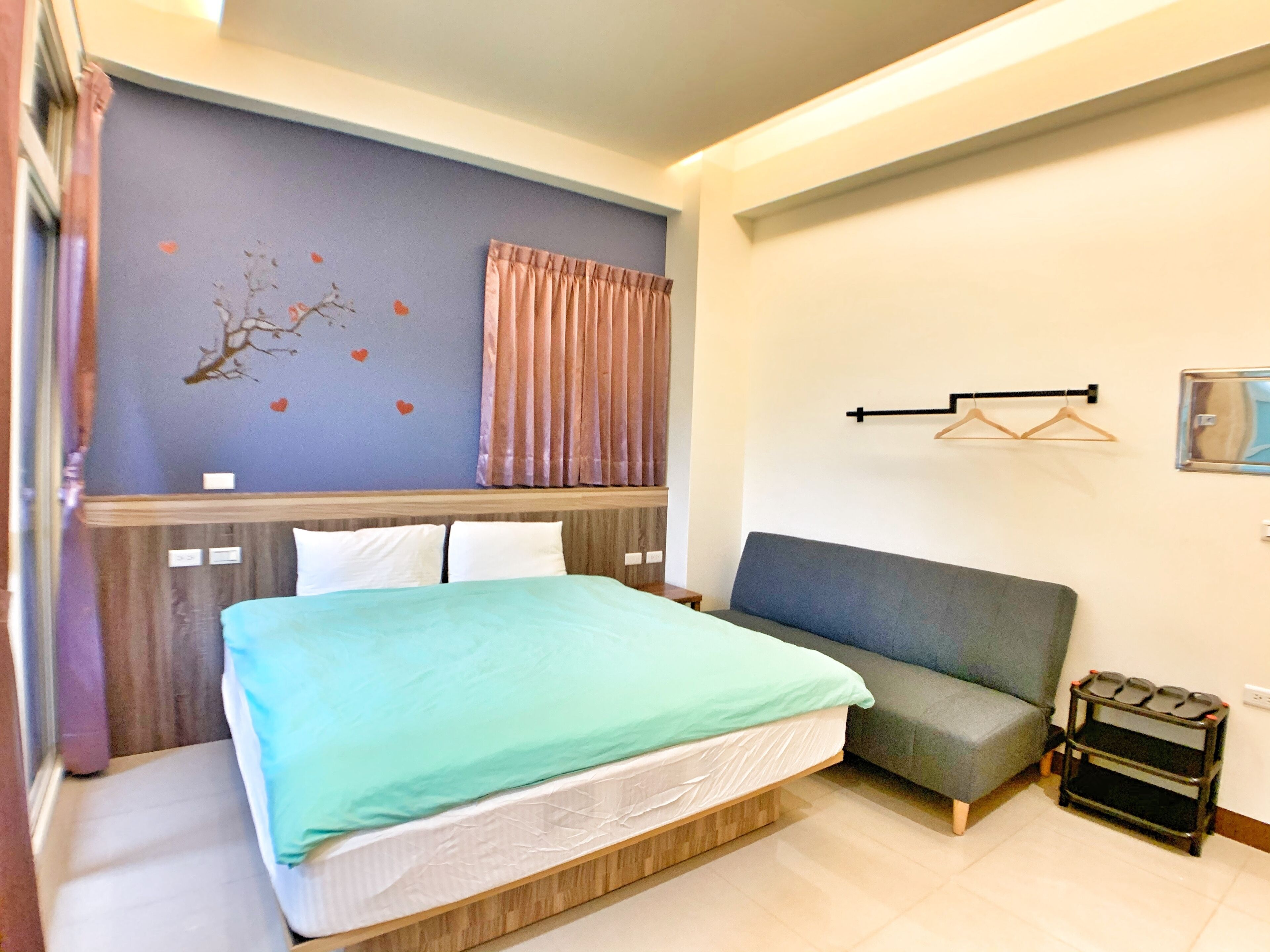 A bedroom with a bed, a sofa, a wall-mounted shelf, and a small table.