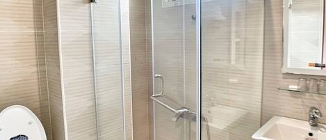 A modern bathroom with a glass-enclosed shower, a white toilet, and a sink with a mirror above it.
