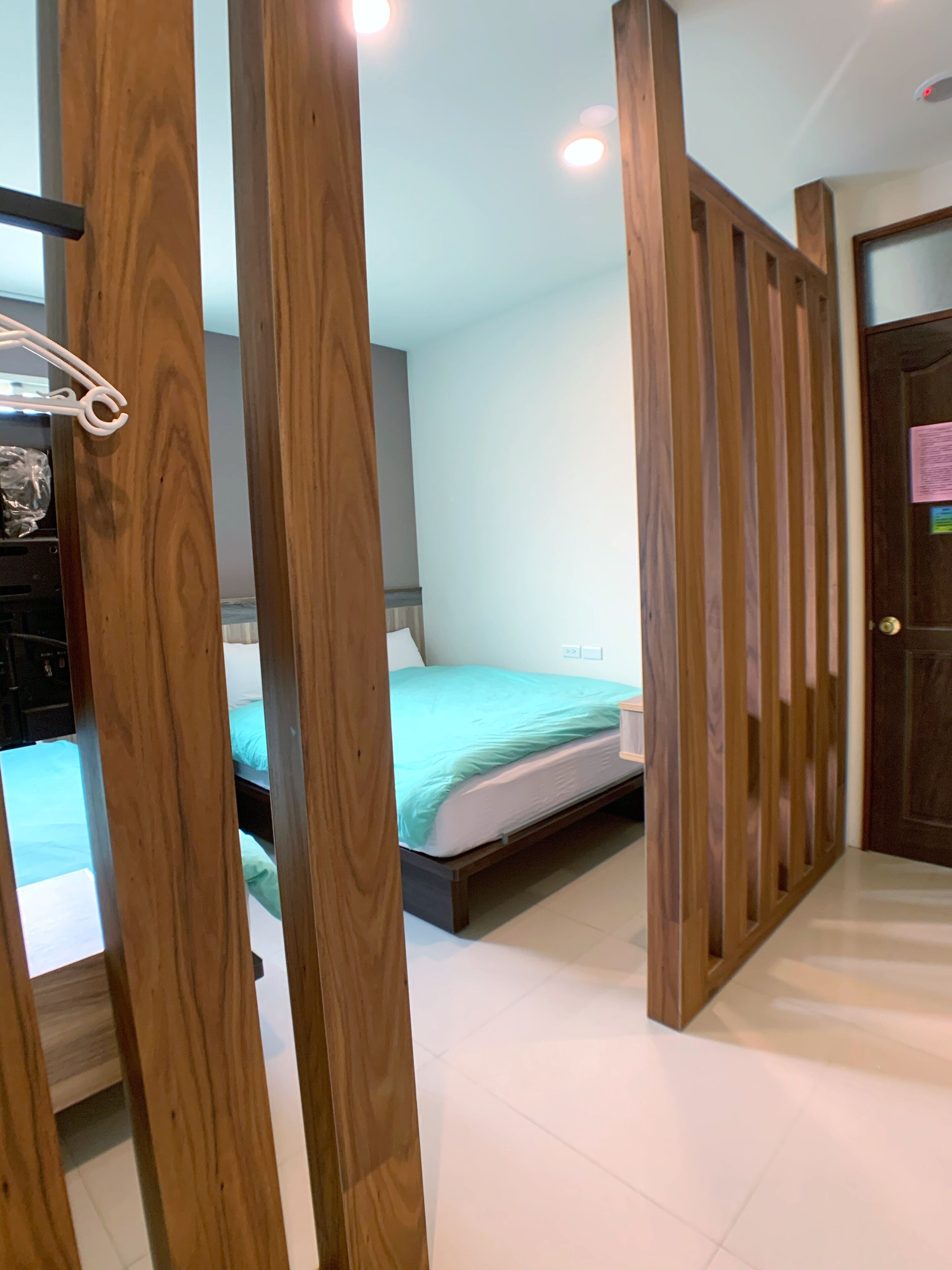 Un dormitorio con un separador de madera, una cama con colcha verde y un armario de madera.