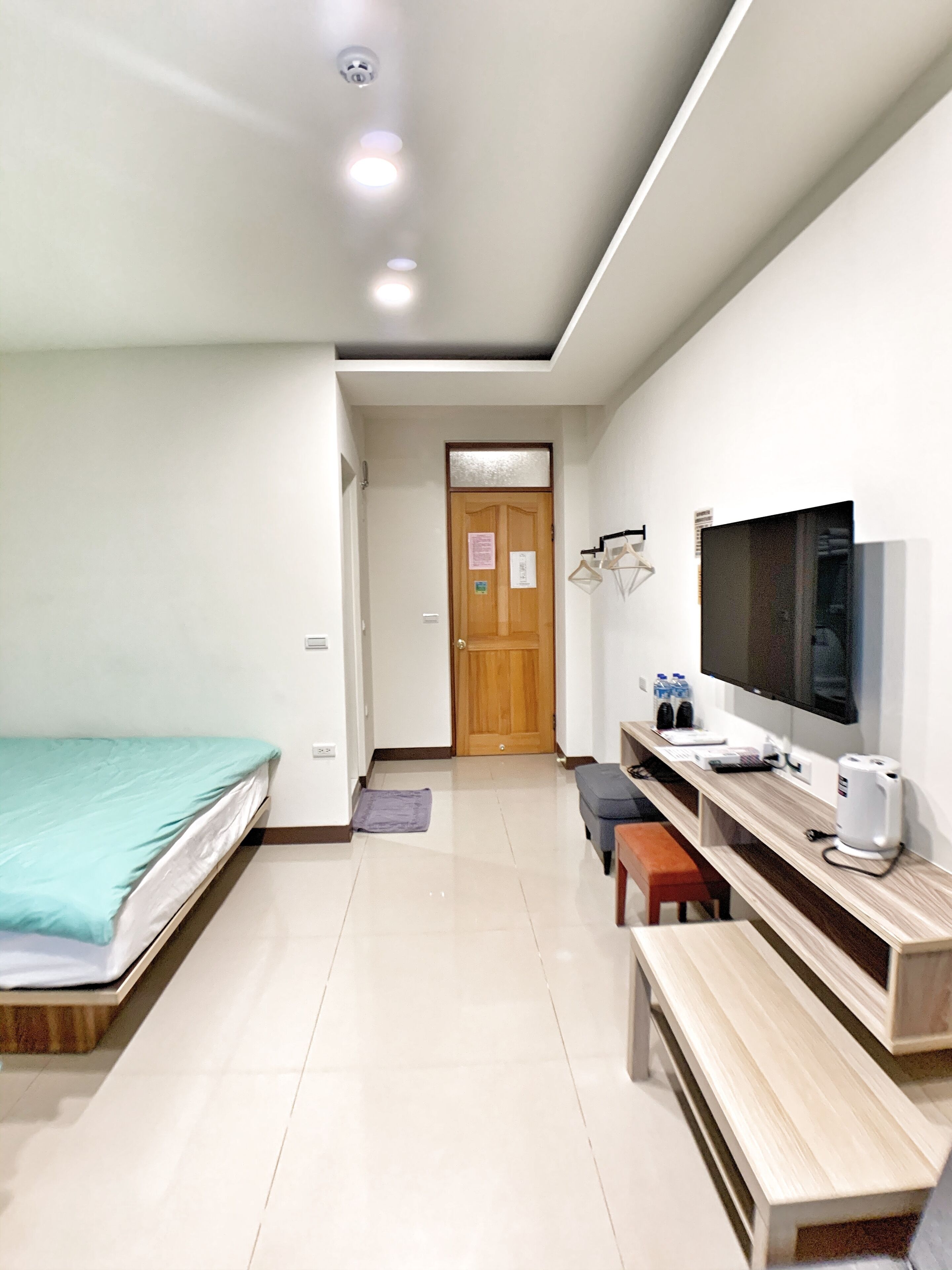 Una habitación de hotel moderna con una cama, un escritorio con ordenador, un televisor y un banco.