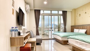 Habitación de hotel con cama, escritorio, silla, una mesita, un banco, televisor y ventana con vistas a la ciudad.