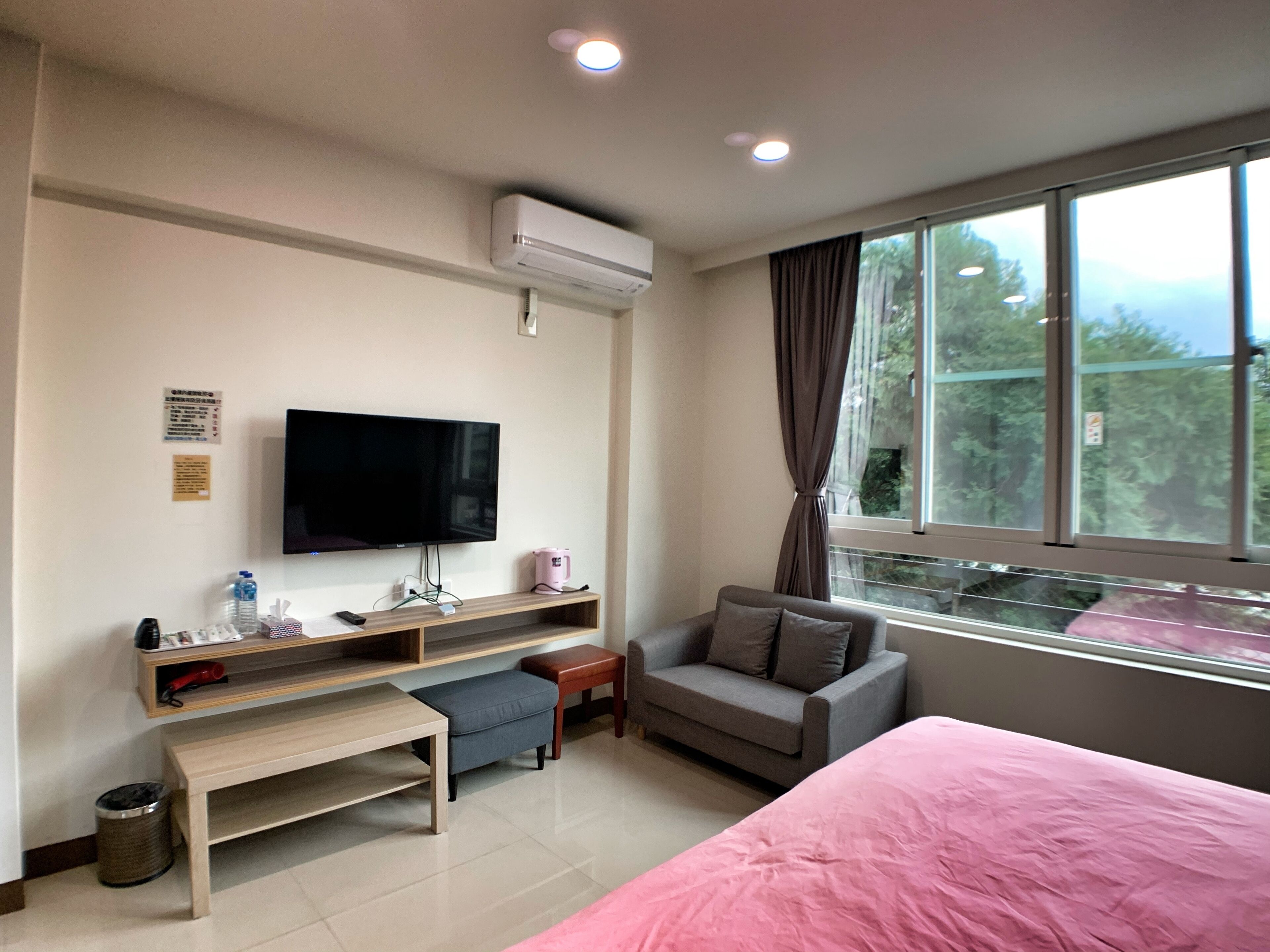 A hotel room with a bed, a television, a desk with a computer, a chair, and a window with a view of trees.
