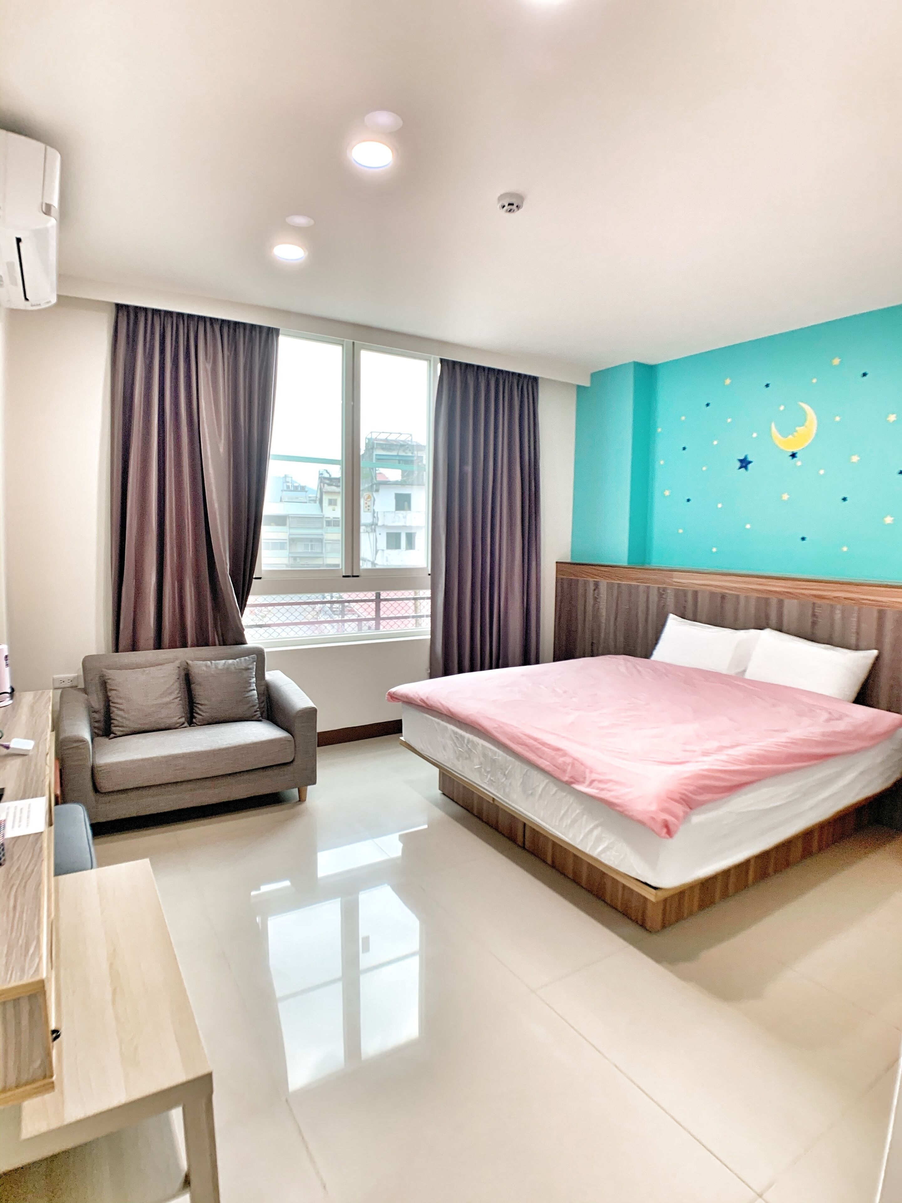 A modern hotel room with a bed, a sofa, a desk, and a window with curtains.
