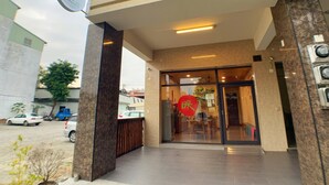 Entrada de un hotel con puerta de cristal, un letrero circular rojo y un estacionamiento visible al fondo.