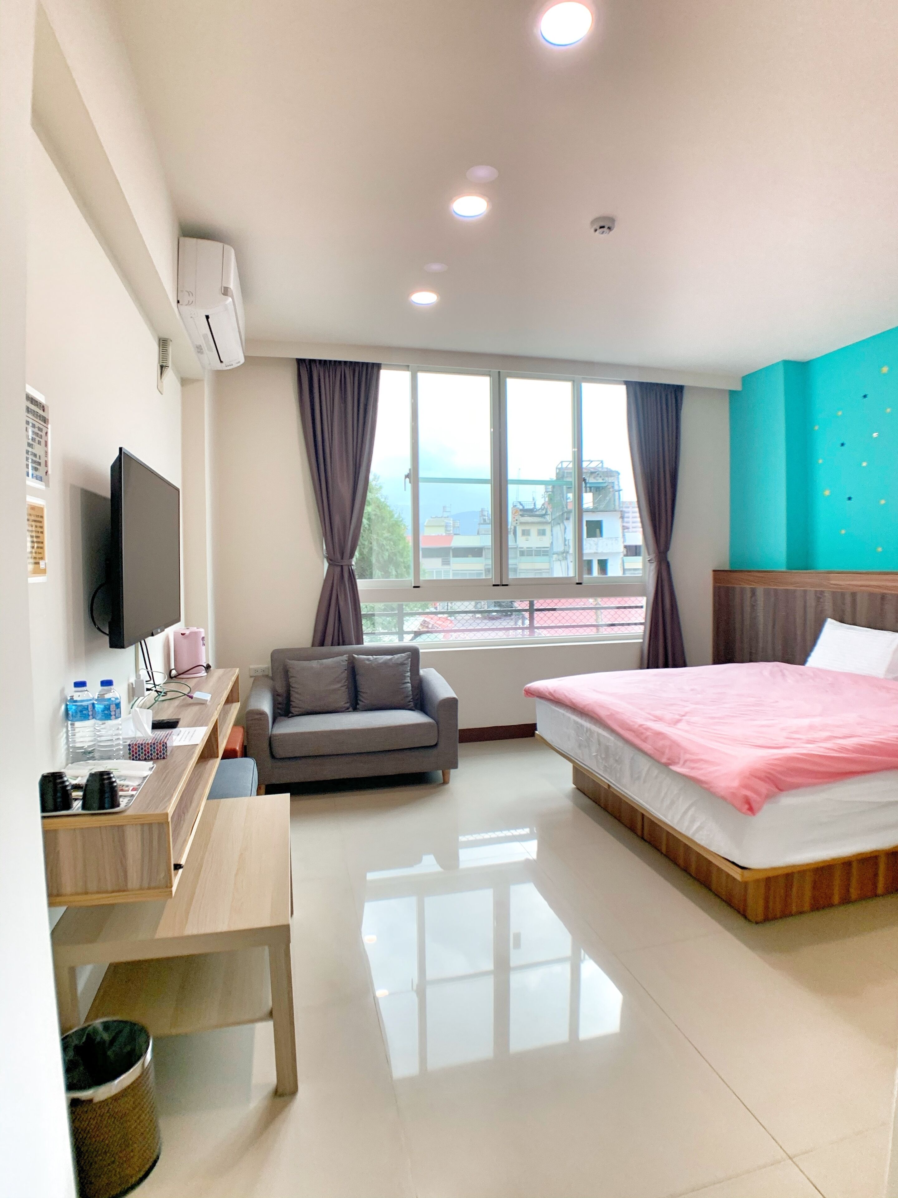 A hotel room with a bed, a desk, a sofa, a TV, and a window with curtains.