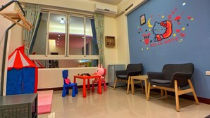 Una sala de juegos infantiles con un adhesivo de pared de Hello Kitty, una litera con dosel a rayas rojas y blancas, y una pequeña mesa llena de juguetes.