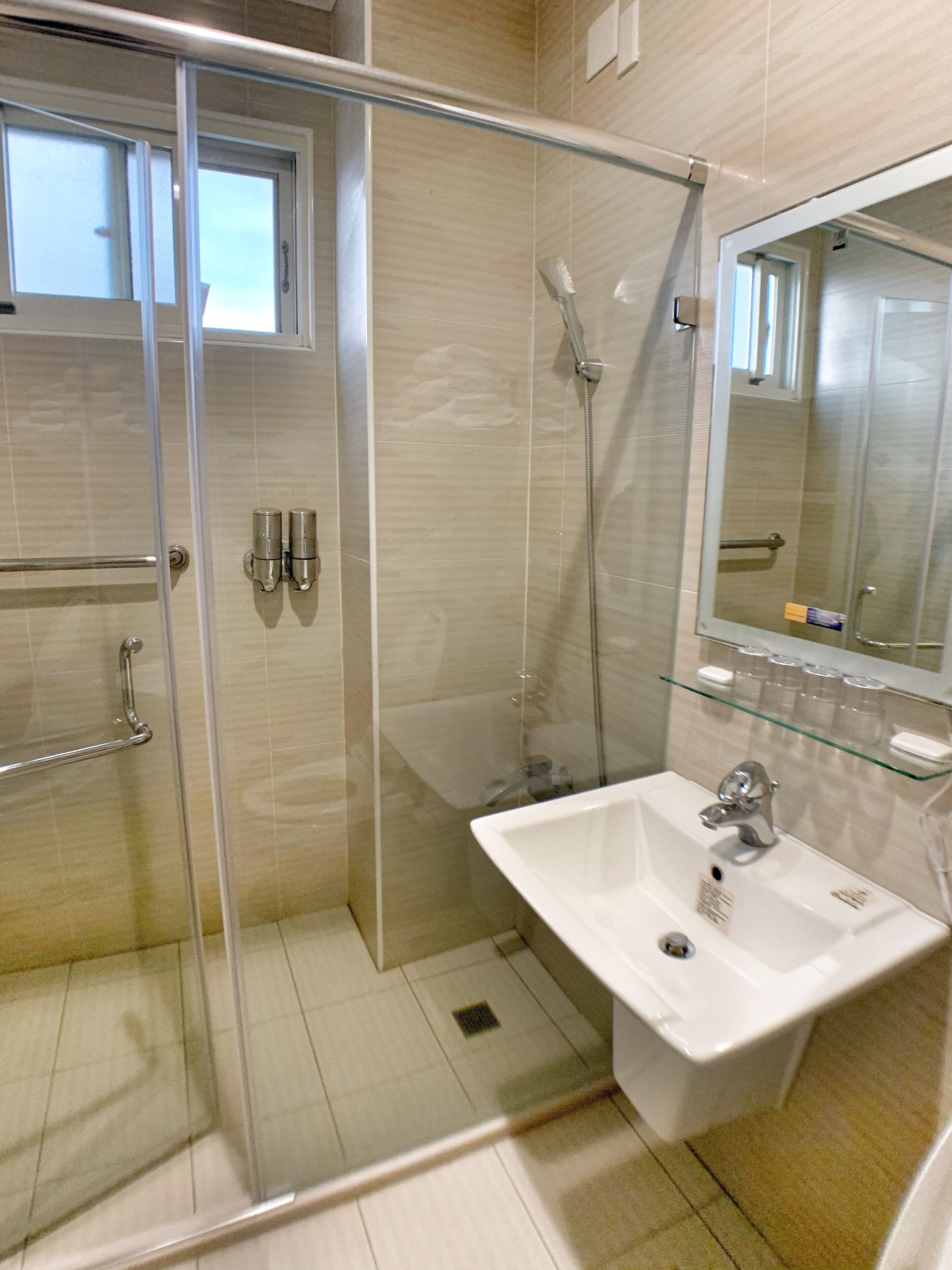 Un baño moderno con ducha de vidrio, un lavamanos blanco y un espejo encima.