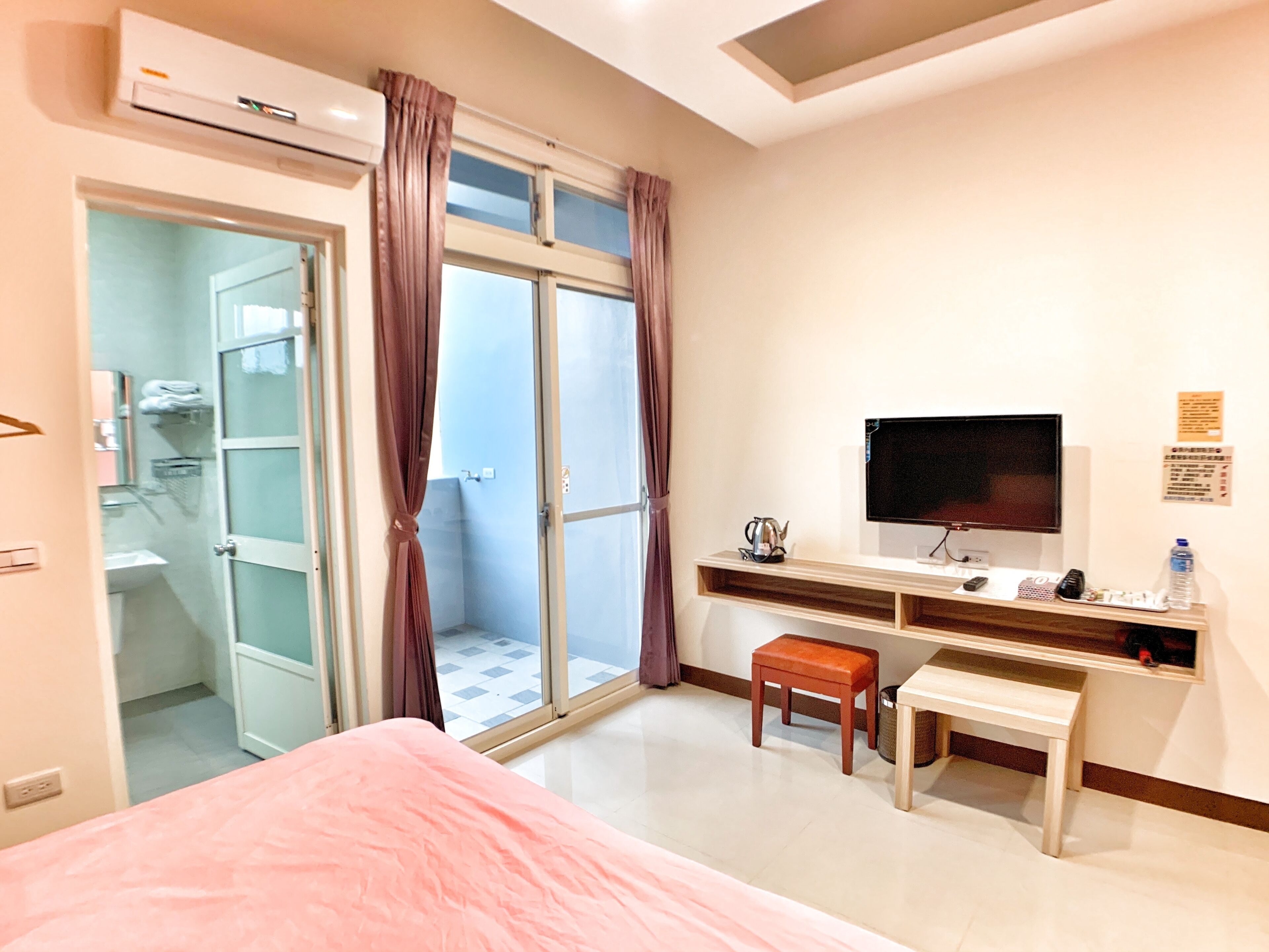 A hotel room with a bed, a desk, a television, and a shower area.
