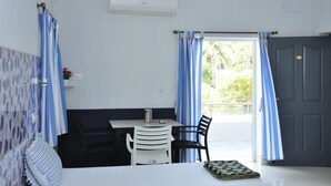 A room with a bed, a table with chairs, a window with curtains, and an air conditioning unit. - Quiet Home Pondy (Vanur)