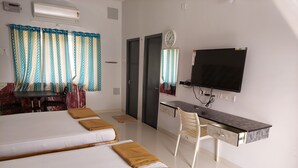 A hotel room with two beds, a desk, a TV, and a clock on the wall. - Quiet Home Pondy (Vanur)