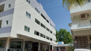 A multi-story hotel with a reception area, outdoor seating, and potted plants. - Quiet Home Pondy (Vanur)