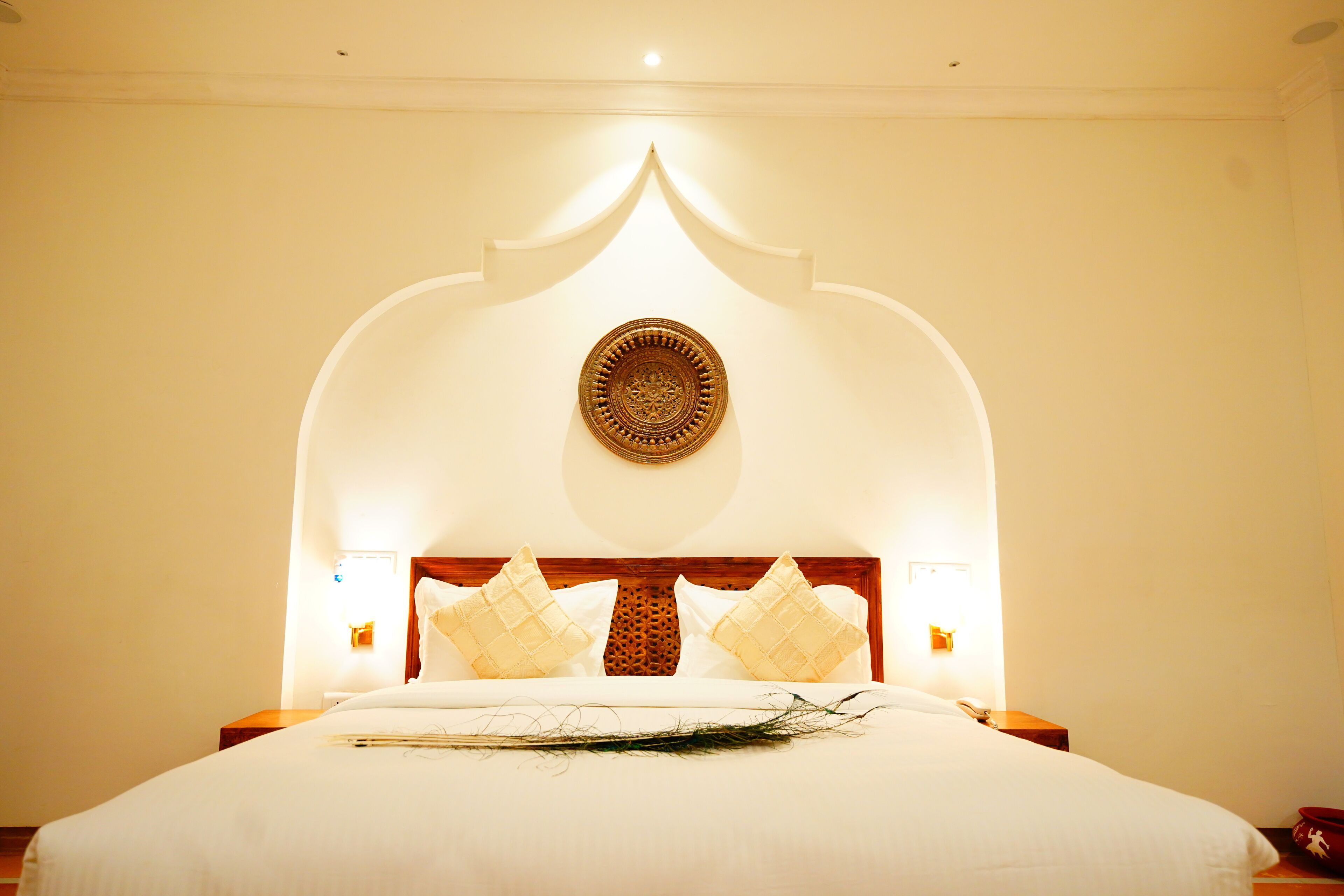 A neatly made bed with a decorative headboard, a wall-mounted decorative plate, and bedside lamps.