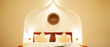 A neatly made bed with a decorative headboard, a wall-mounted decorative plate, and bedside lamps.