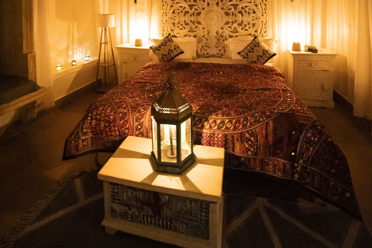 Een kamer met een bed, nachtkastje, lamp en een hanglamp.