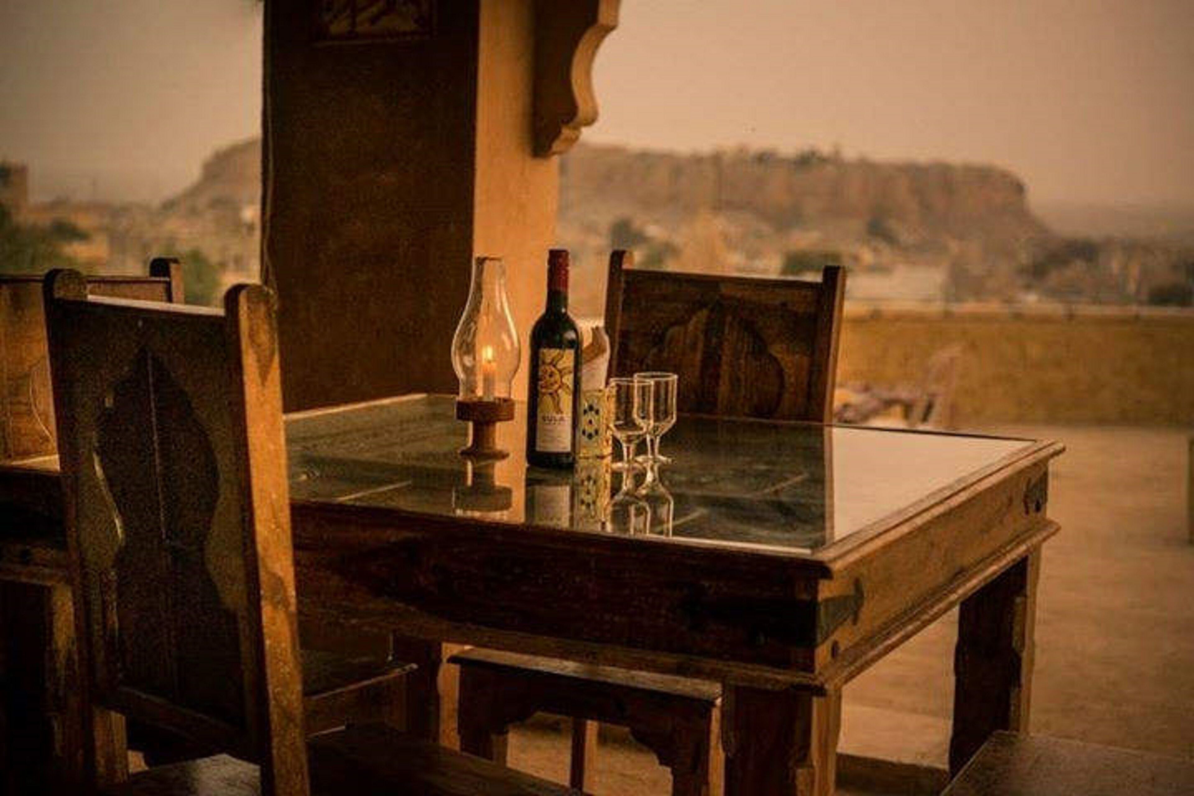 A table with a bottle and glasses, set against a view of a landscape.
