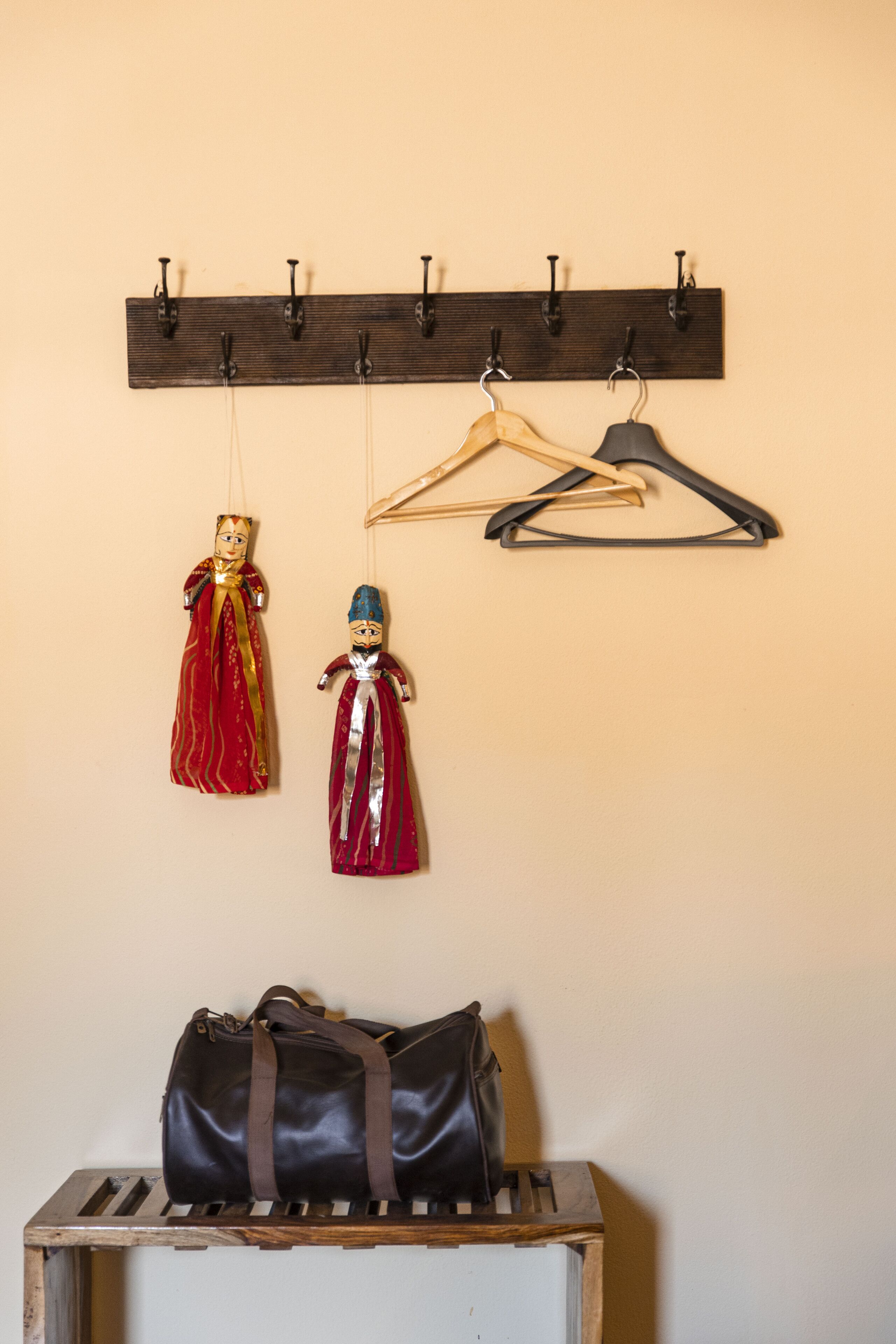 A wooden coat rack with two dolls and a handbag hanging on it.