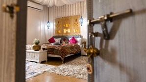 Een kamer met een bed, nachtkastje, decoratieve hanglamp en een deur met een messing handvat.