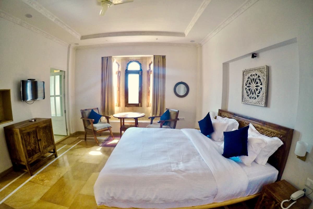 Een hotelkamer met een groot bed, een bureau, een stoel, een televisie en een raam met gordijnen.
