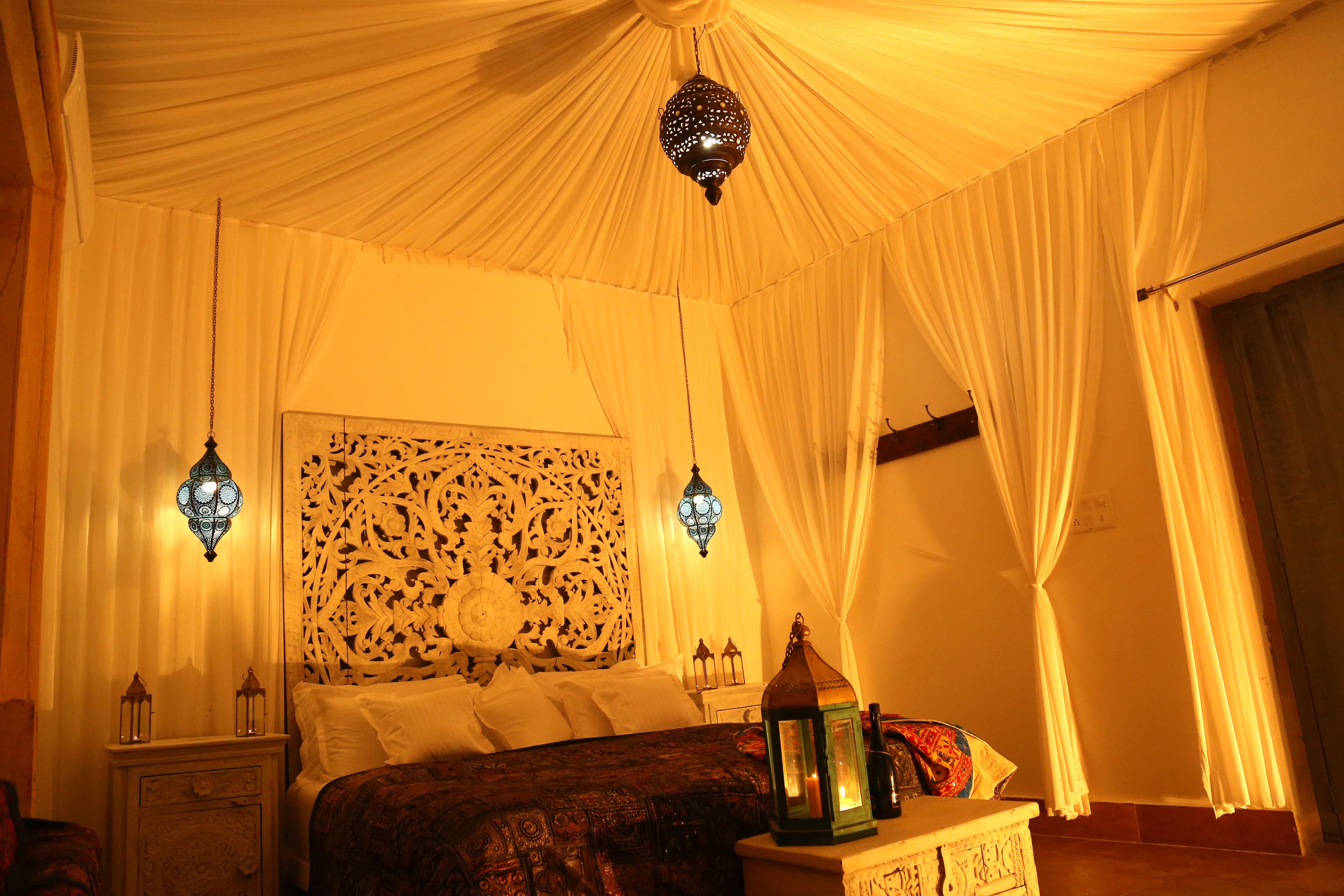 Una habitación con cama, mesita de noche, decoración en la pared y faroles colgantes.