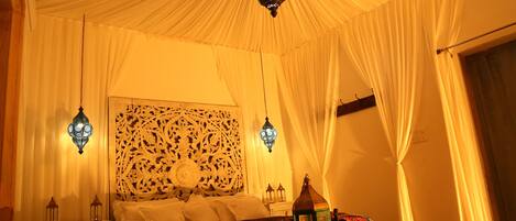 Una habitación con cama, mesita de noche, decoración en la pared y faroles colgantes.