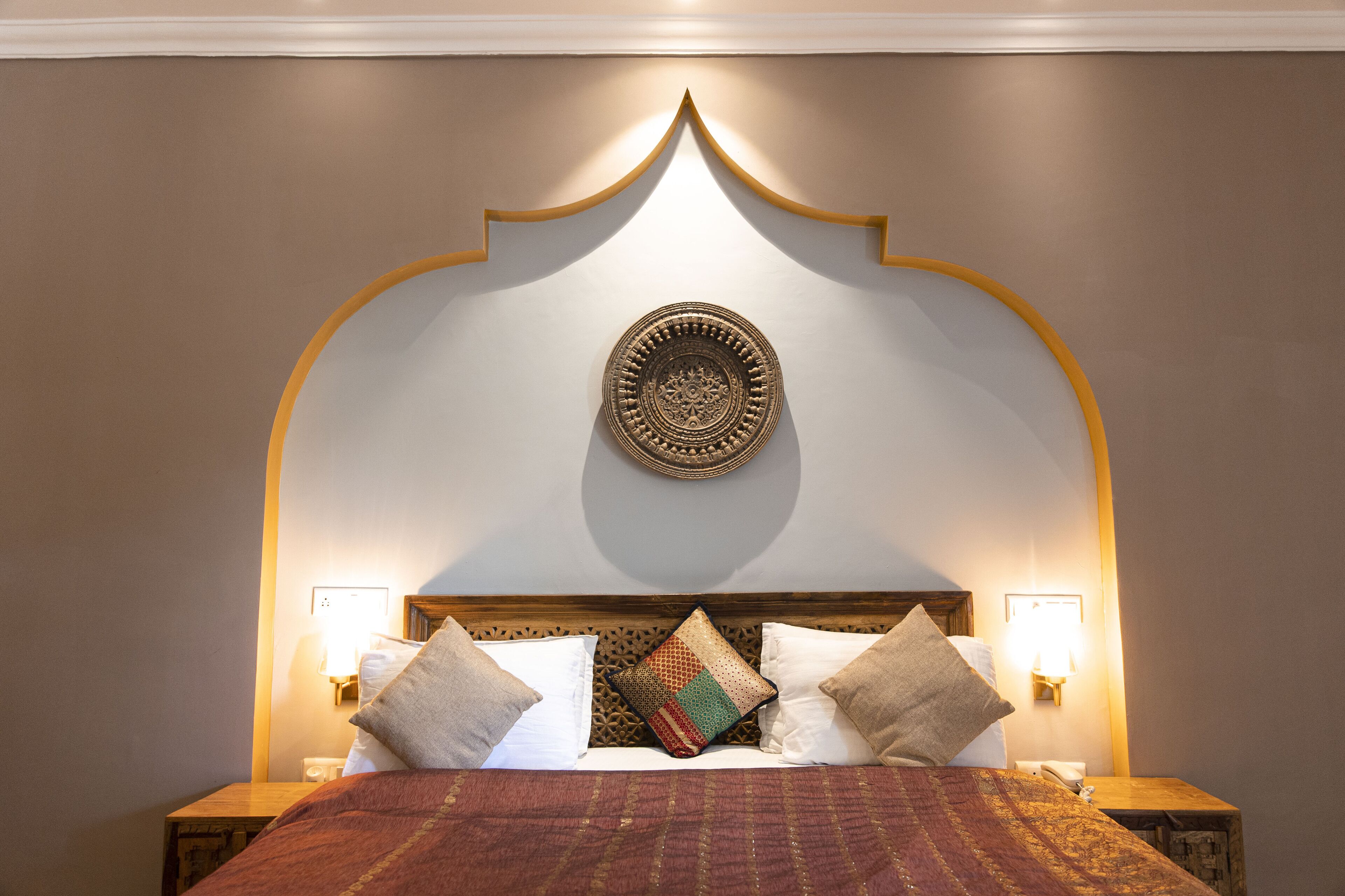 A bed with a patterned headboard, two bedside lamps, and a decorative wall piece above it.