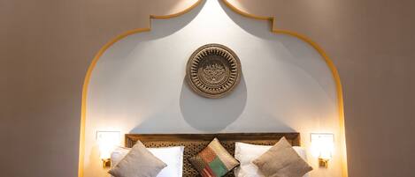 A bed with a patterned headboard, two bedside lamps, and a decorative wall piece above it.