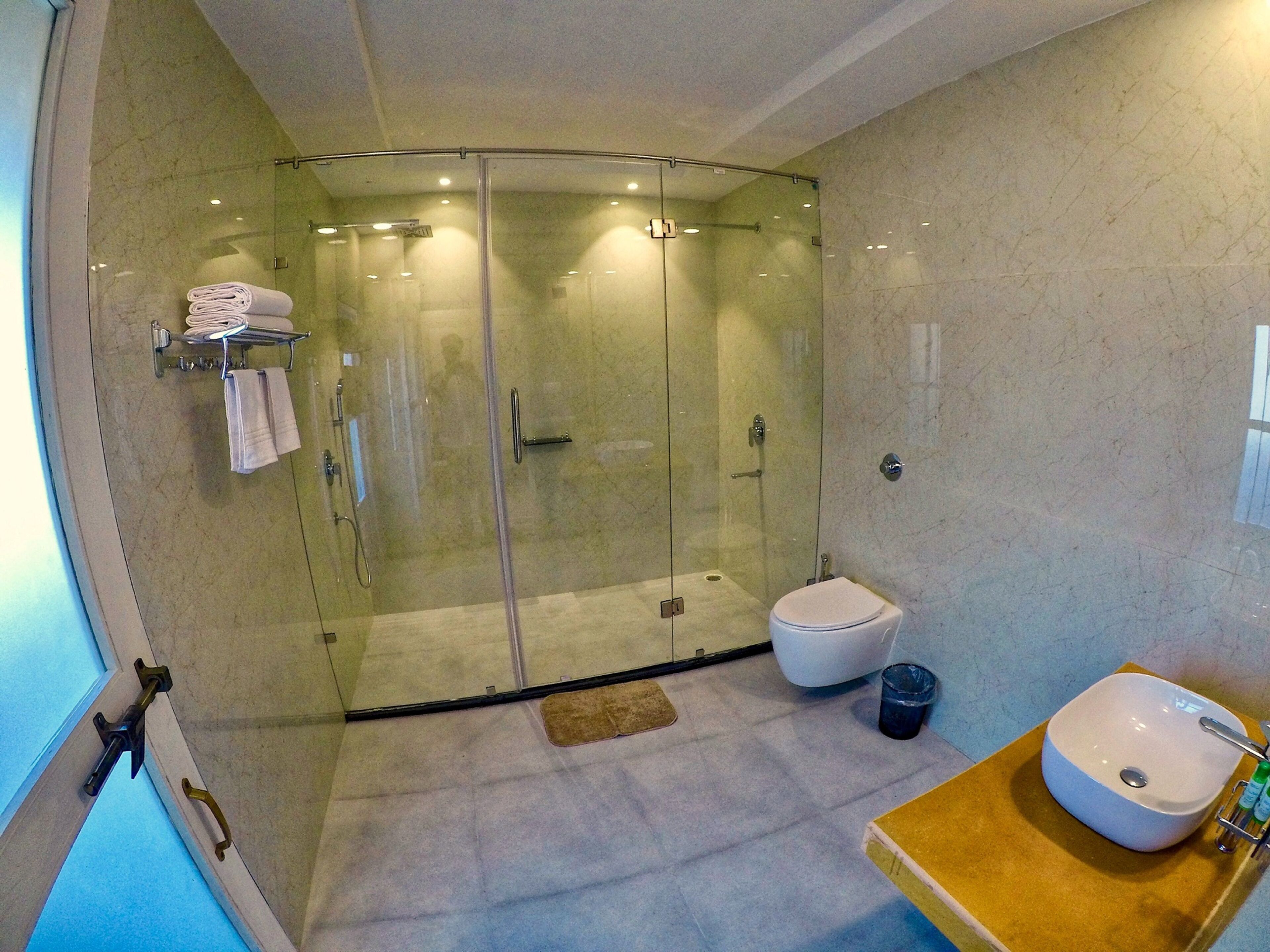 A modern bathroom with a glass-enclosed shower, a toilet, and a sink with a towel rack.