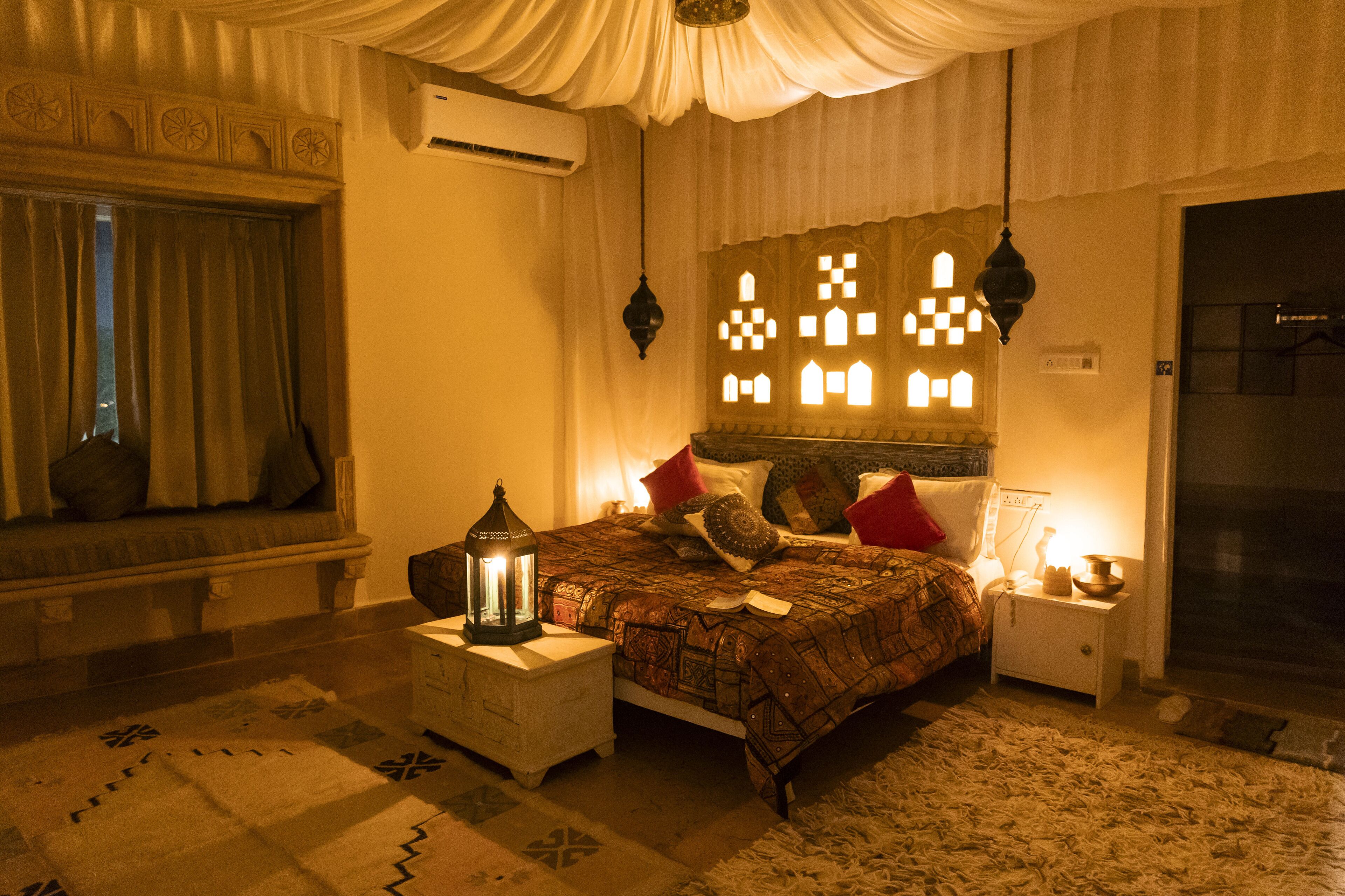 Une chambre à coucher avec un lit, une table de chevet, une lampe et une fenêtre avec des rideaux.