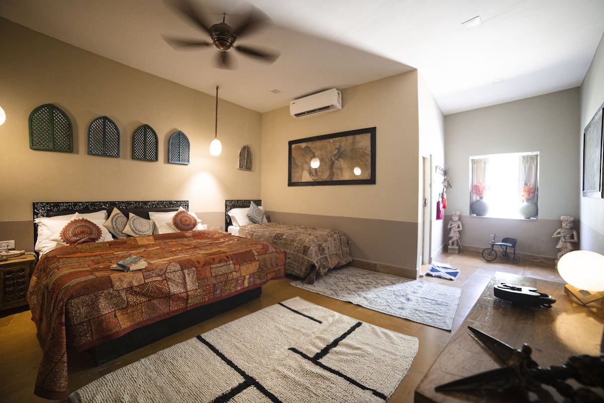Een slaapkamer met een groot bed, twee kleinere bedden, een plafondventilator en een raam met gordijnen.