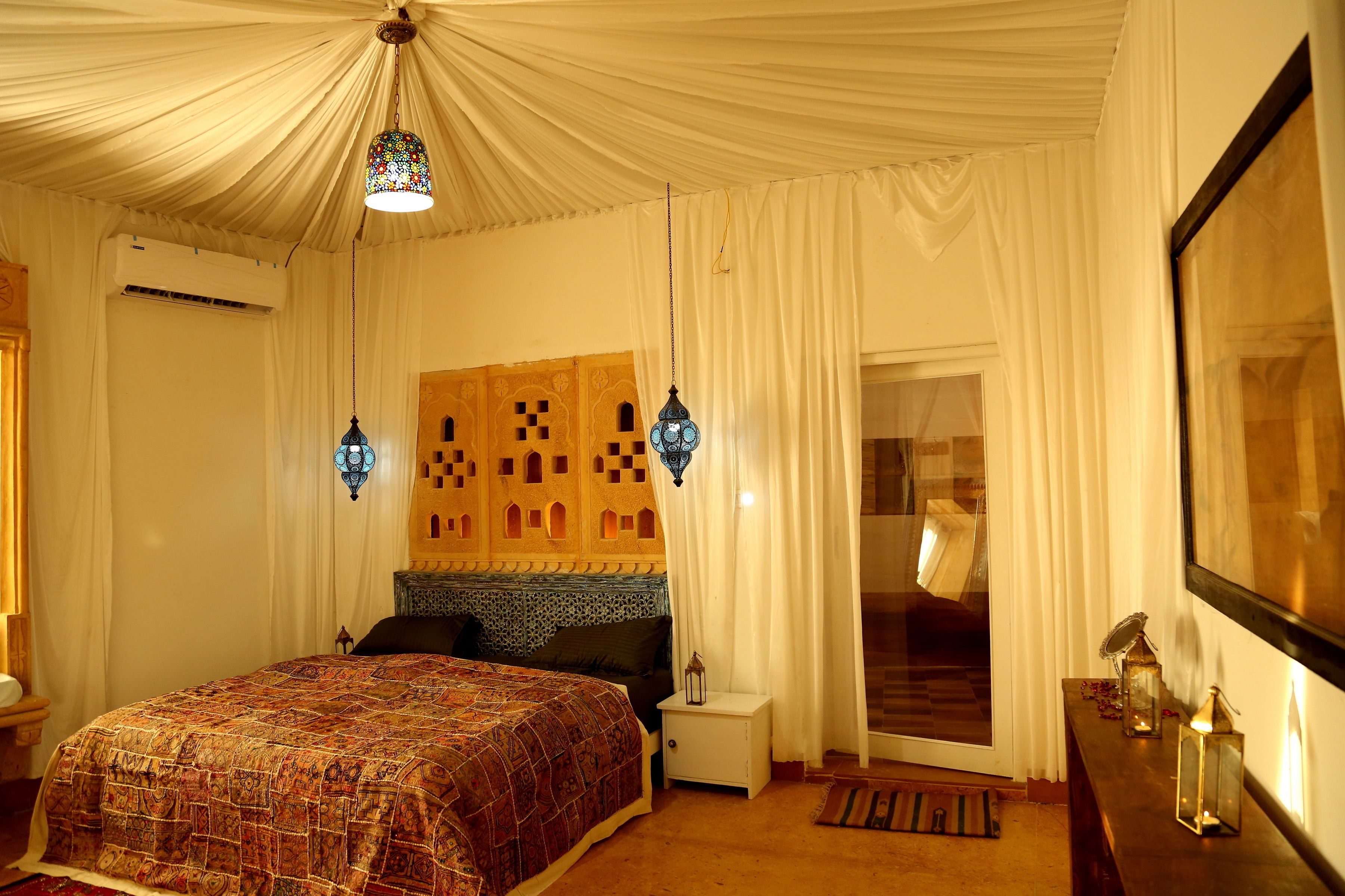 A bedroom with a patterned bedspread, a headboard with a geometric design, a hanging lantern, and a large mirror on the wall.