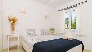 Ein Schlafzimmer mit einem Bett, Nachttischen, einem Fenster mit Vorhängen und Wandleuchten.