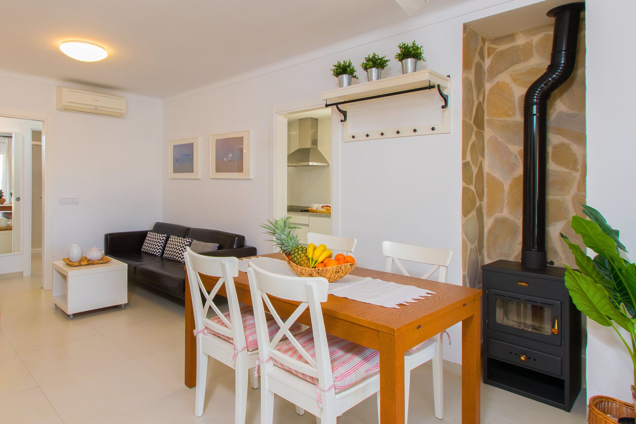Un coin repas avec une table et des chaises en bois, un canapé blanc et une cuisine visible à travers une porte ouverte.