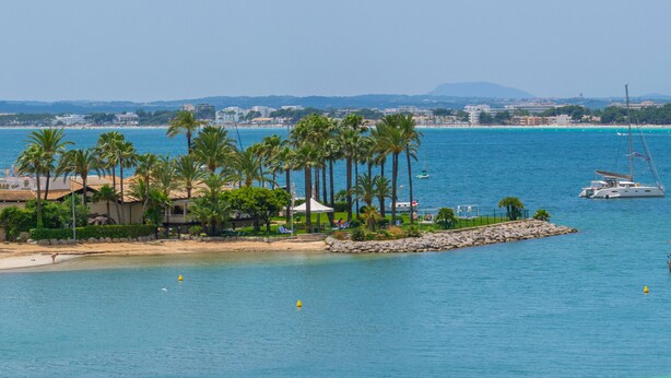 Eine Küstenlandschaft mit Strand, Palmen und einer Yacht im Wasser.