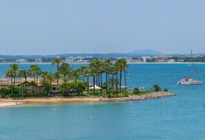 Un paysage côtier avec une plage, des palmiers et un yacht sur l’eau.