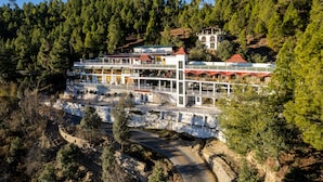 A multi-story hotel with a white exterior and red roofs, situated on a hillside with dense forest in the background. - Hotel Robinsson Palace (Kosiyakutoli)