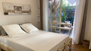A wooden bed with white bedding, a wall-mounted artwork, and a view of the outdoors through a glass door.