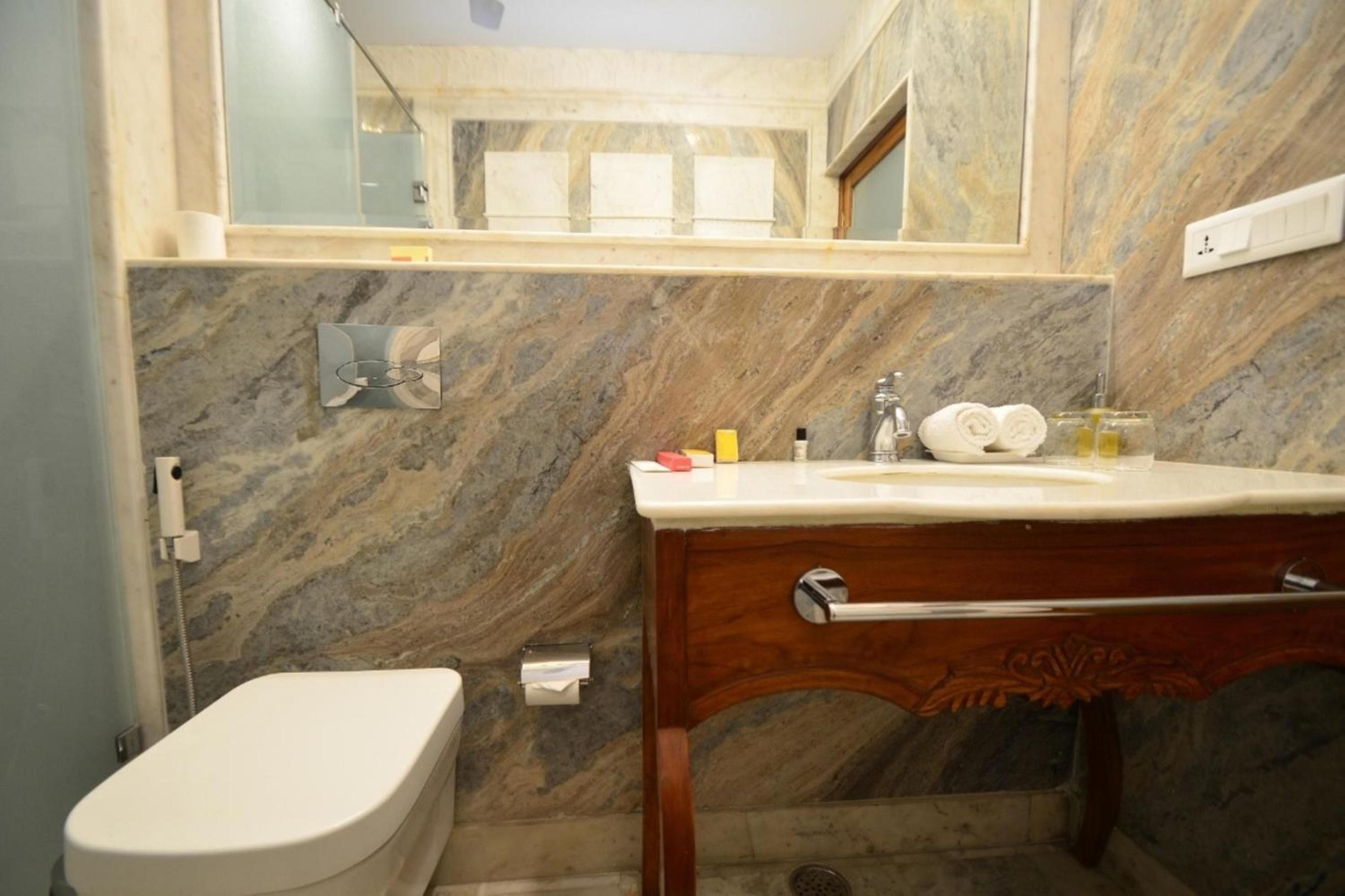 Une salle de bain avec un mur en marbre, un meuble-lavabo en bois, des toilettes et un miroir.