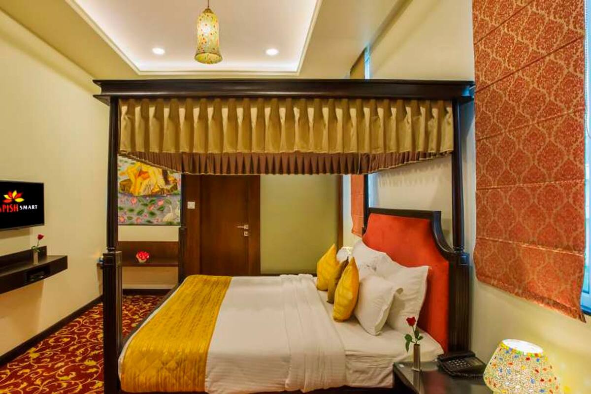 A hotel room with a four-poster bed, a television on the wall, and a decorative painting above the bed.